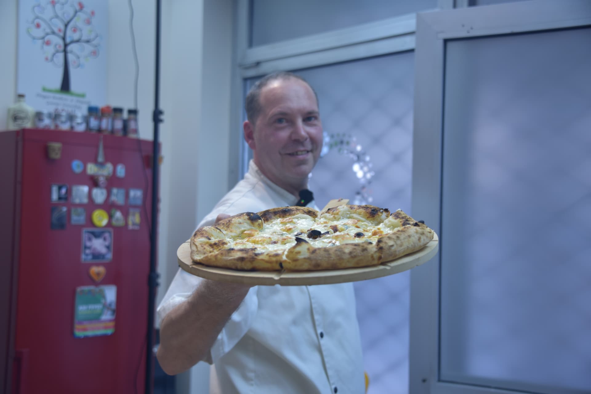 Nasmejani pizza majstor pokazuje belu picu sa mocarelom