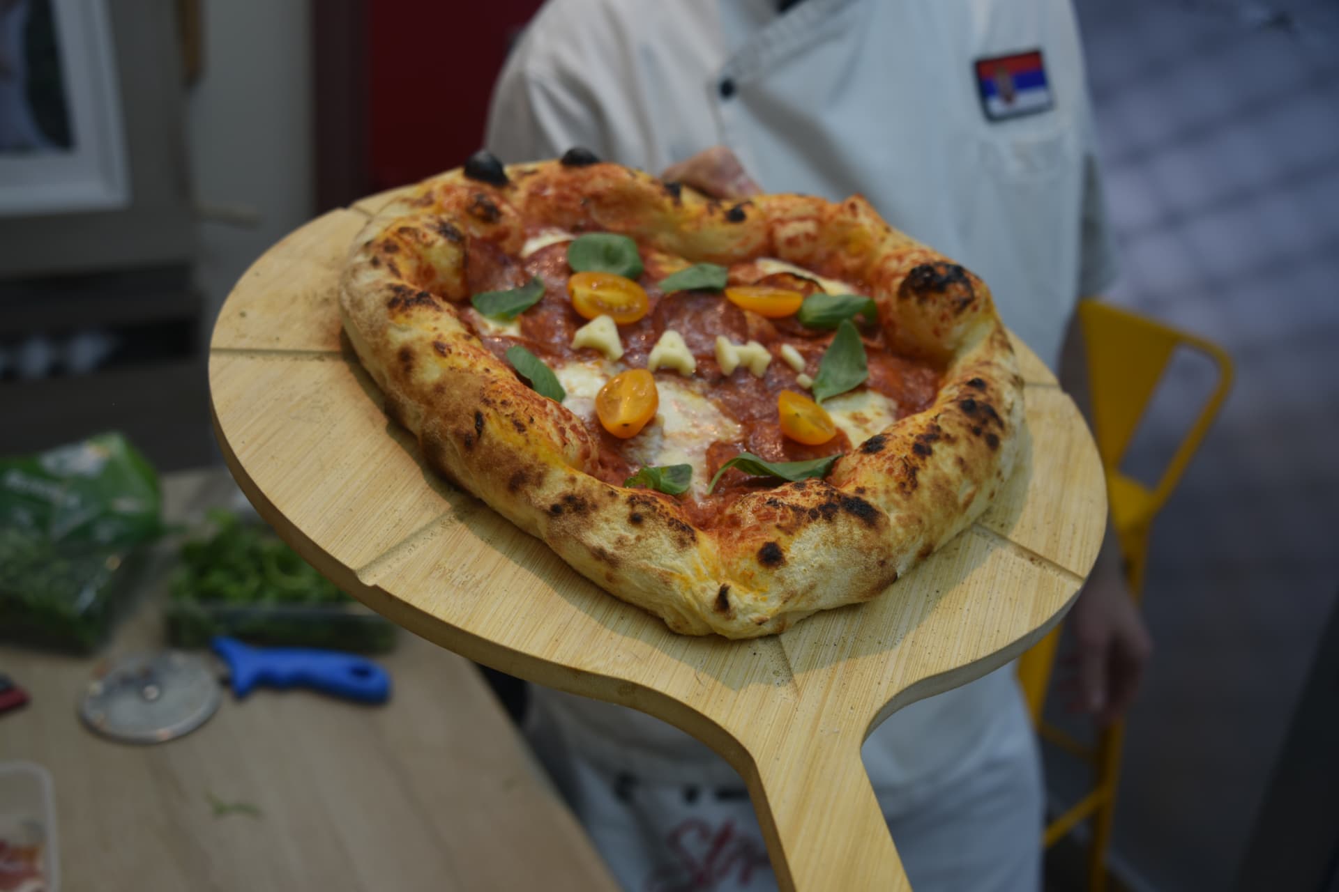 Pizza majstor drži gotovu napolitana picu na drvenoj lopati